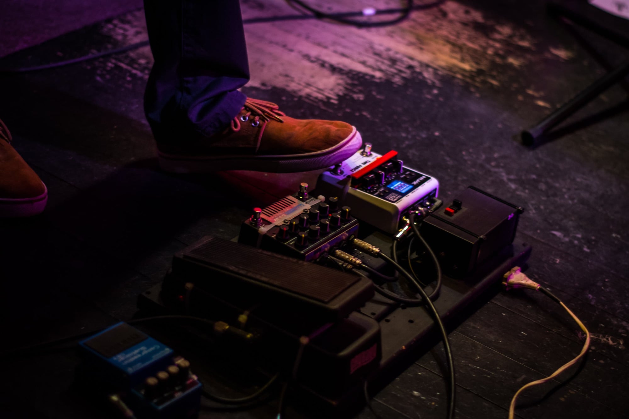 a guitarist wearing brown shoes is using effects pedals during practice