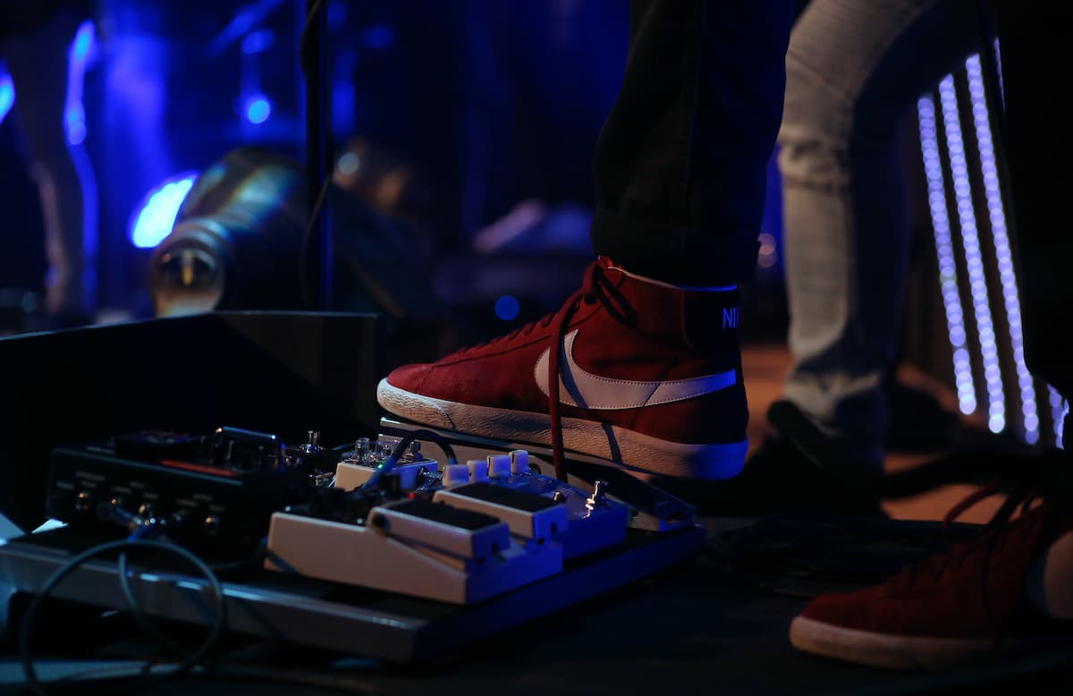 a guitarist wearing a nike shoes stomping his feet to stompboxes